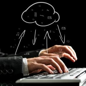 Businessman typing on the keyboard of his computer synchronizing files with the cloud storage with a hand-drawn cloud icon with data transfer arrows.